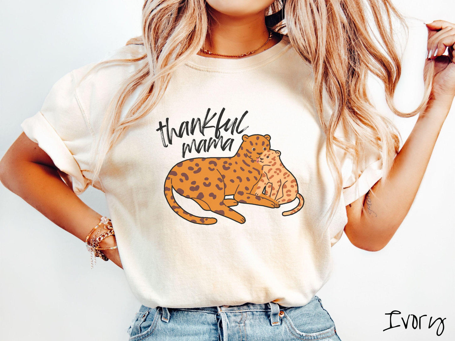 A woman wearing a cute, vintage ivory colored Comfort Colors T-shirt with the text thankful mama in black, sharpie font. Below is an orange, mother leopard coddling its child.