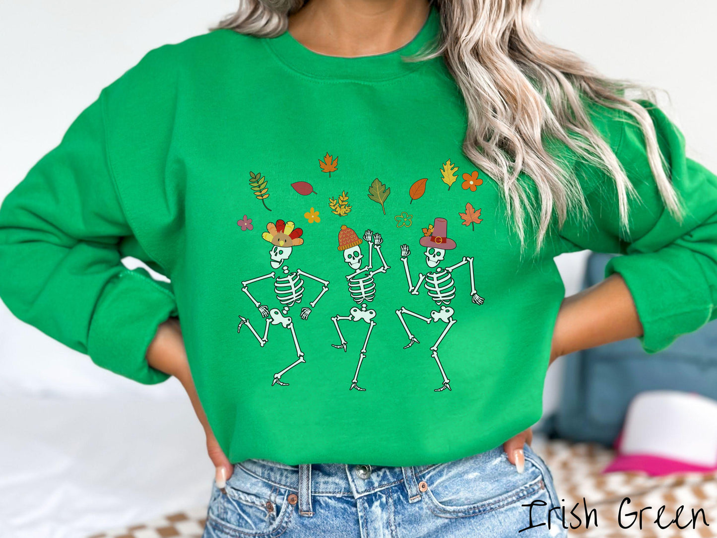 A woman wearing a cute irish
green colored sweatshirt with three white skeletons wearing pilgrim hats dancing with colorful fall leaves in the air.