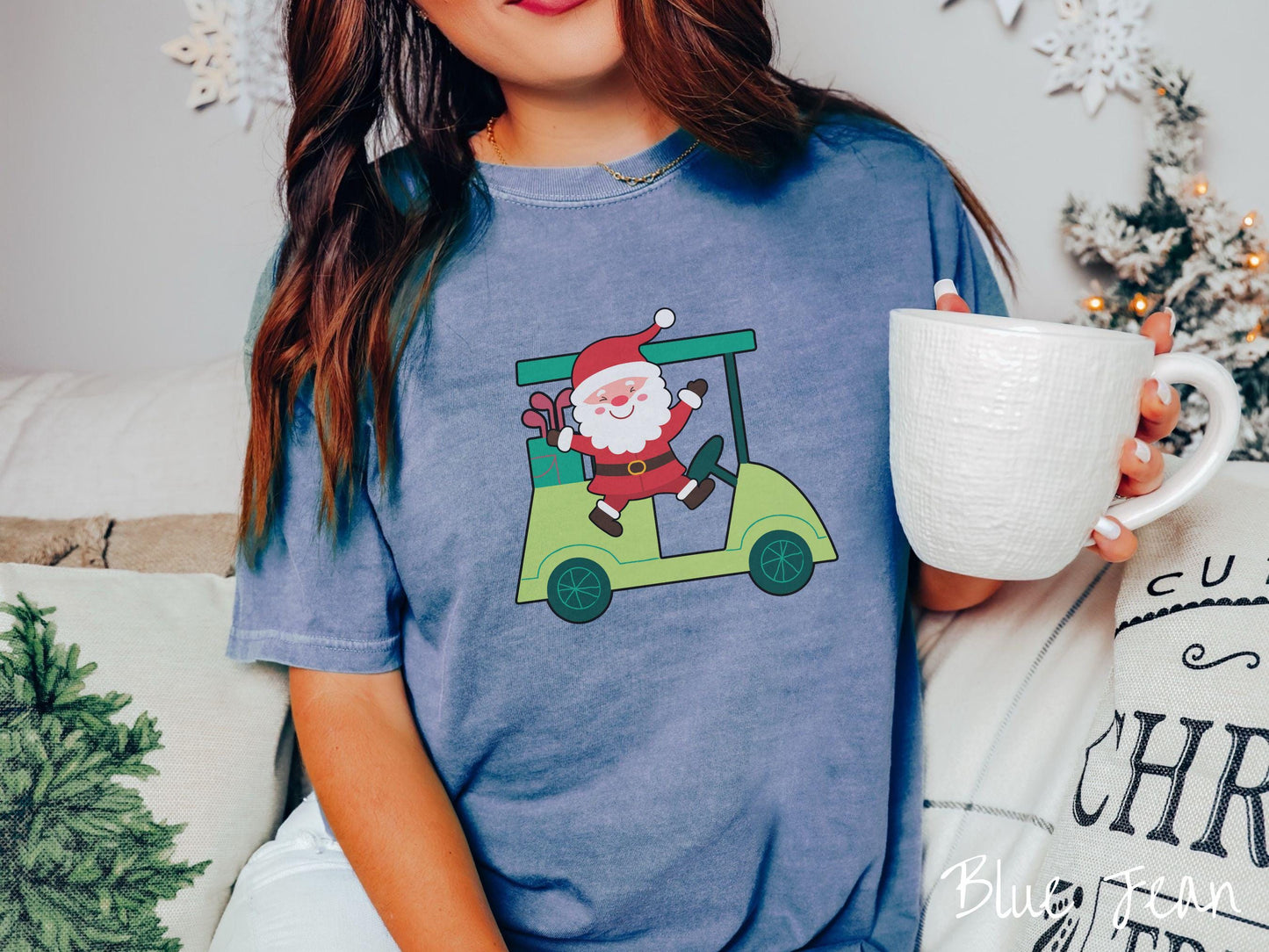 A woman wearing a cute blue jean colored shirt with smiling Santa driving a green golf cart and waving with both hands.