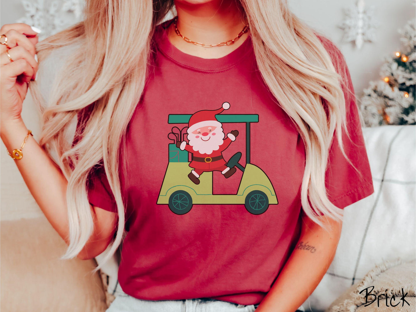 A woman wearing a cute brick colored shirt with smiling Santa driving a green golf cart and waving with both hands.
