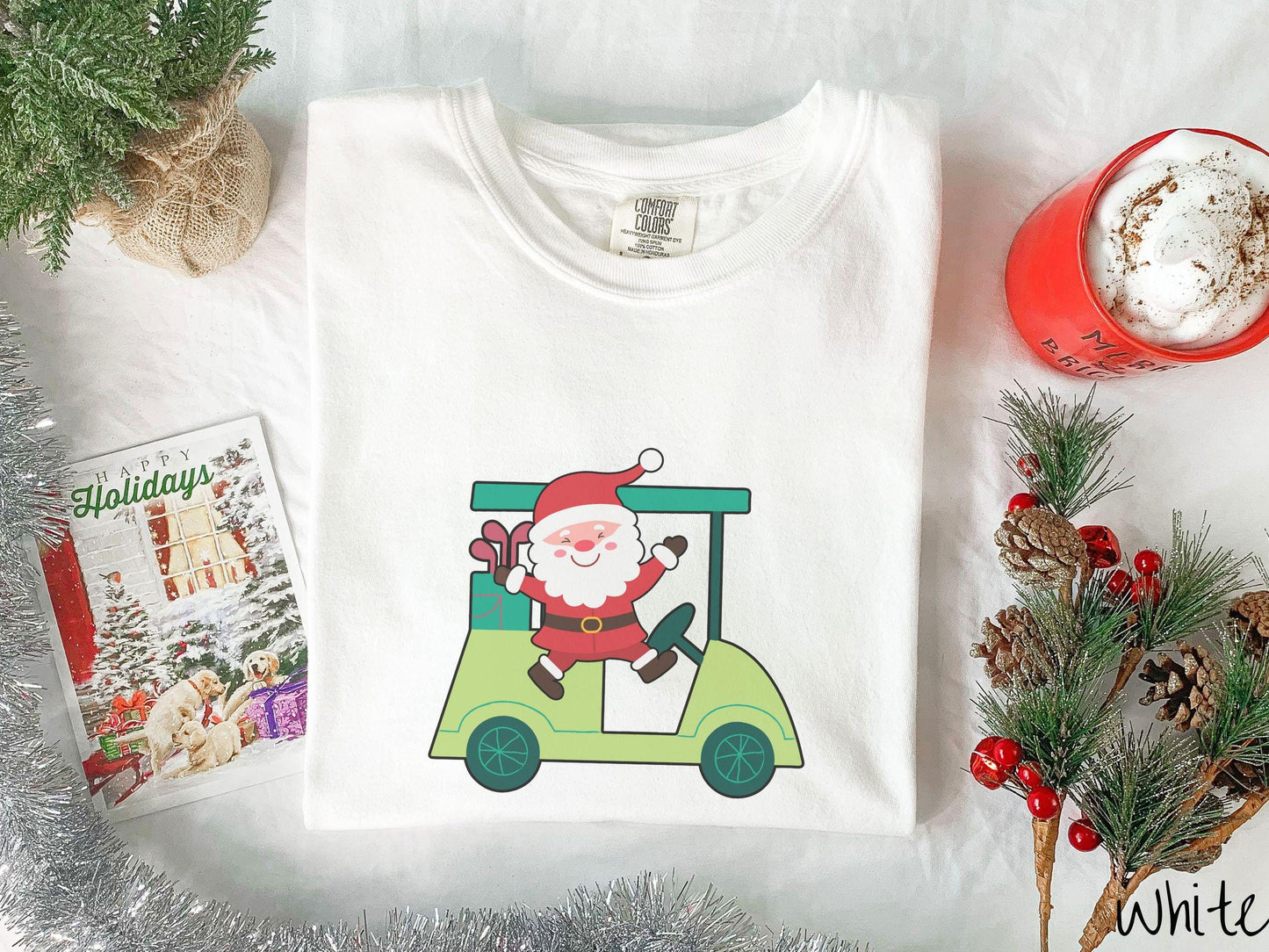 A woman wearing a cute white colored shirt with smiling Santa driving a green golf cart and waving with both hands.