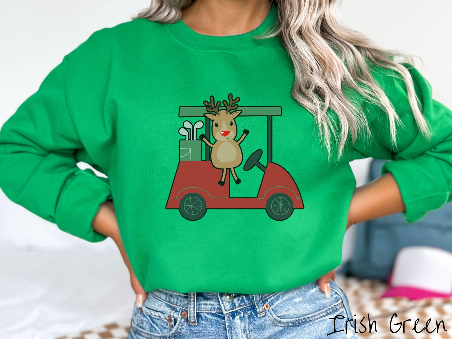 A woman wearing a cute irish green colored sweatshirt with smiling reindeer driving a red golf cart and waving with both hands.