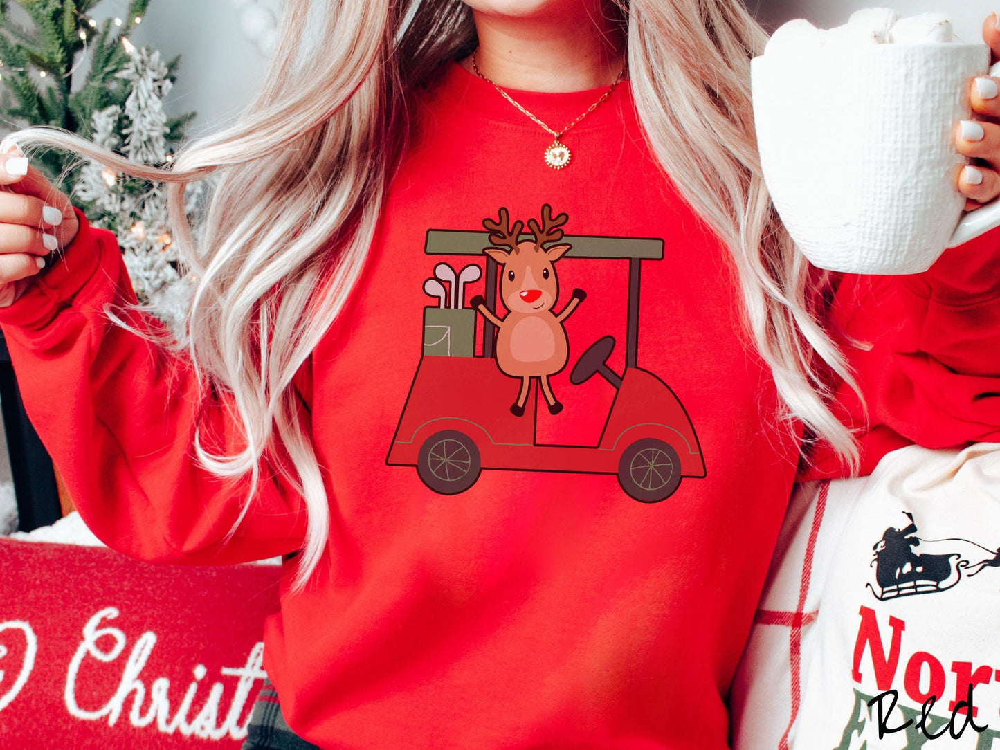 A woman wearing a cute red colored sweatshirt with smiling reindeer driving a red golf cart and waving with both hands.