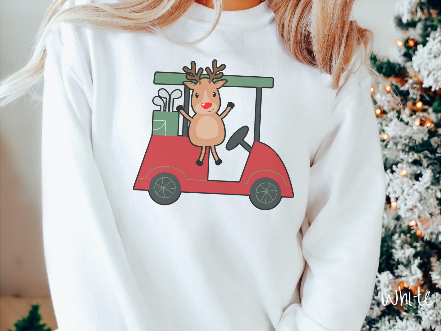 A woman wearing a cute white colored sweatshirt with smiling reindeer driving a red golf cart and waving with both hands.