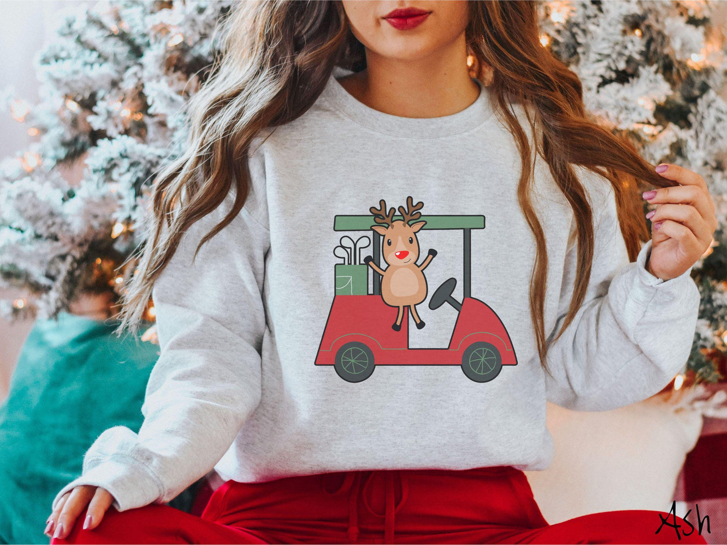A woman wearing a cute ash colored sweatshirt with smiling reindeer driving a red golf cart and waving with both hands.