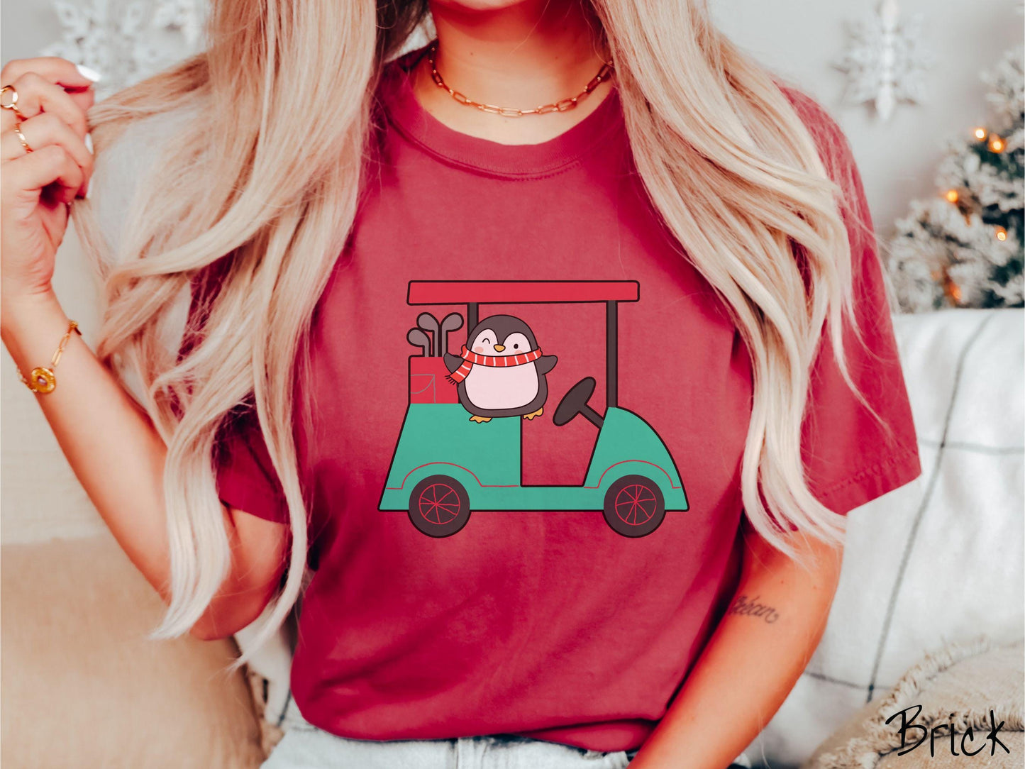 A woman wearing a cute brick colored shirt with smiling penguin driving a green golf cart and waving with both hands.