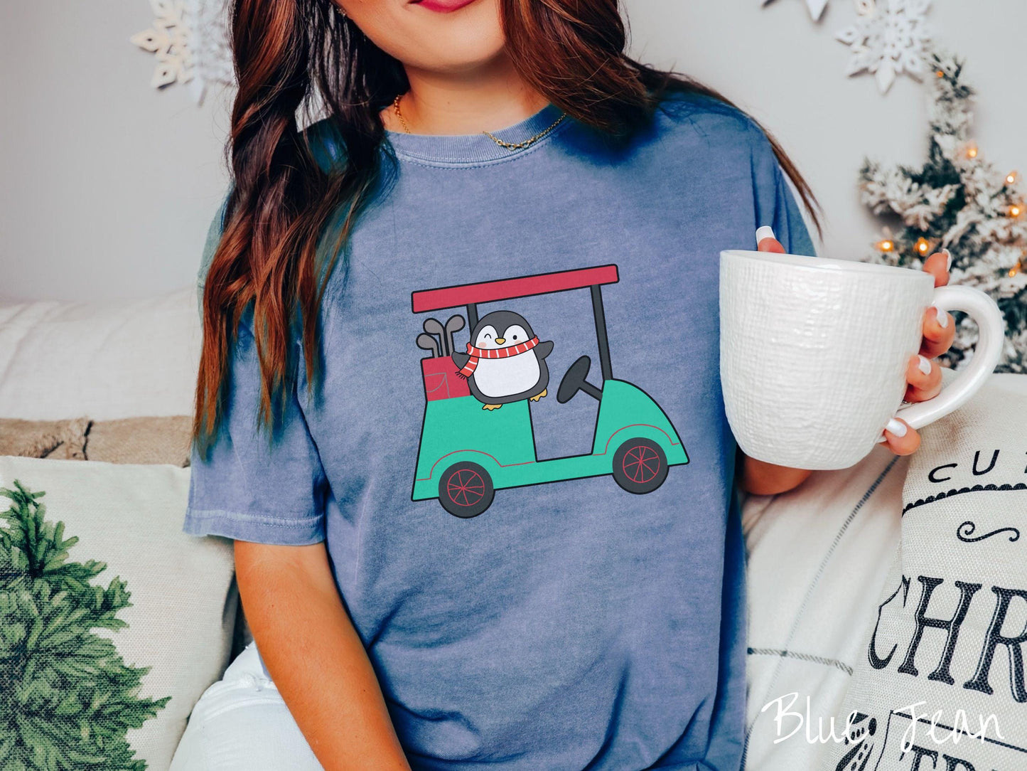 A woman wearing a cute blue jean colored shirt with smiling penguin driving a green golf cart and waving with both hands.