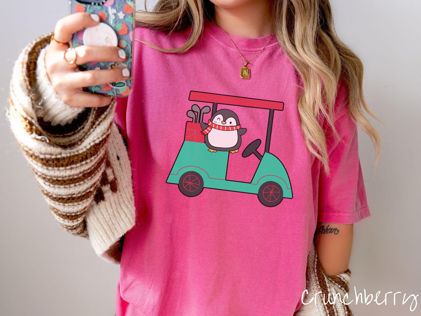 A woman wearing a cute crunchberry colored shirt with smiling penguin driving a green golf cart and waving with both hands.