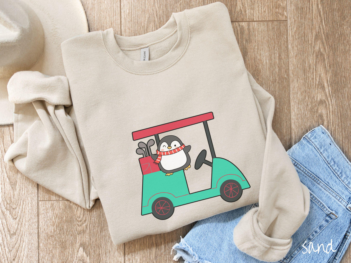 A woman wearing a cute sand colored sweatshirt with smiling penguin driving a green golf cart and waving with both hands.