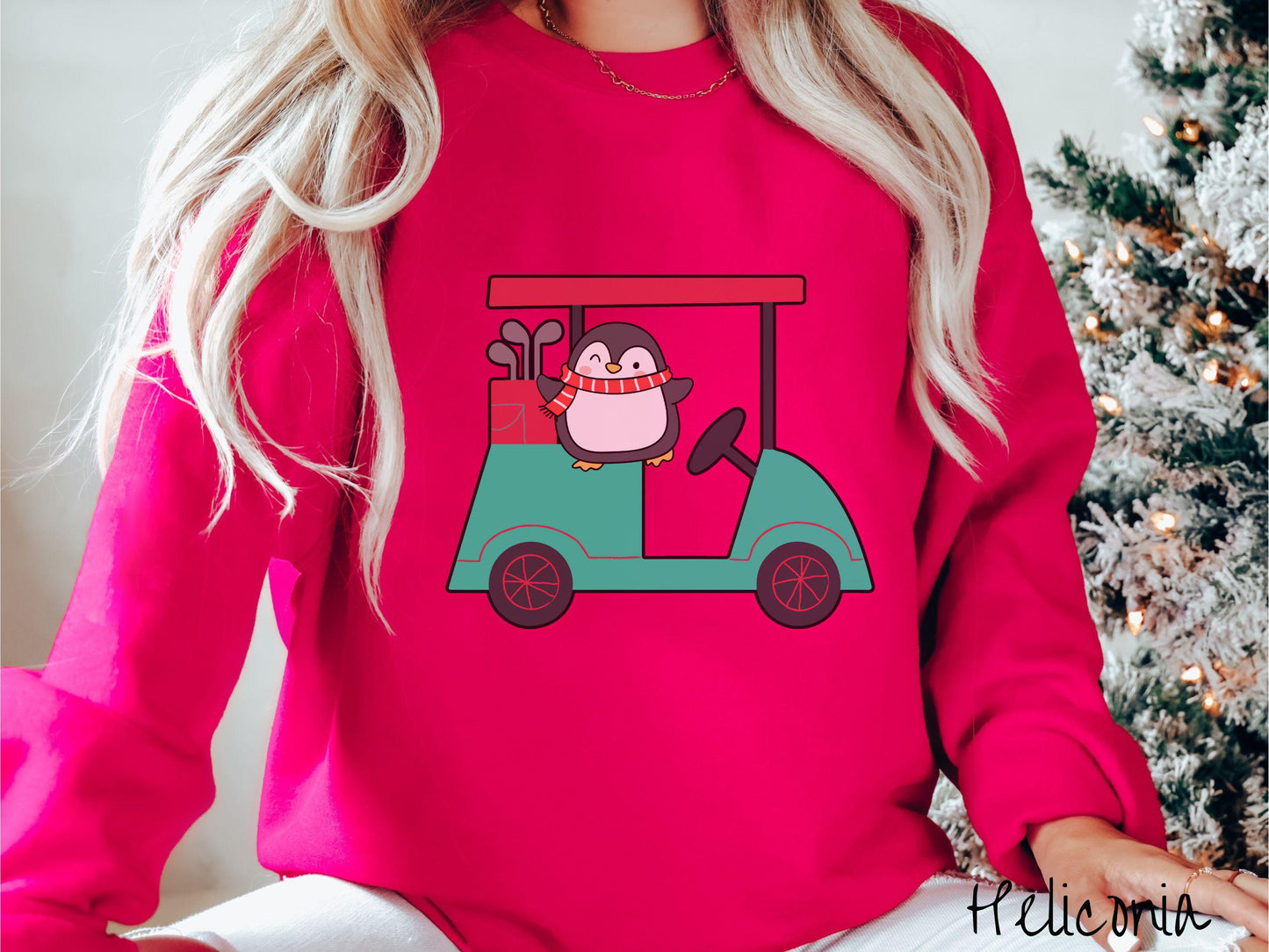 A woman wearing a cute heliconia colored sweatshirt with smiling penguin driving a green golf cart and waving with both hands.