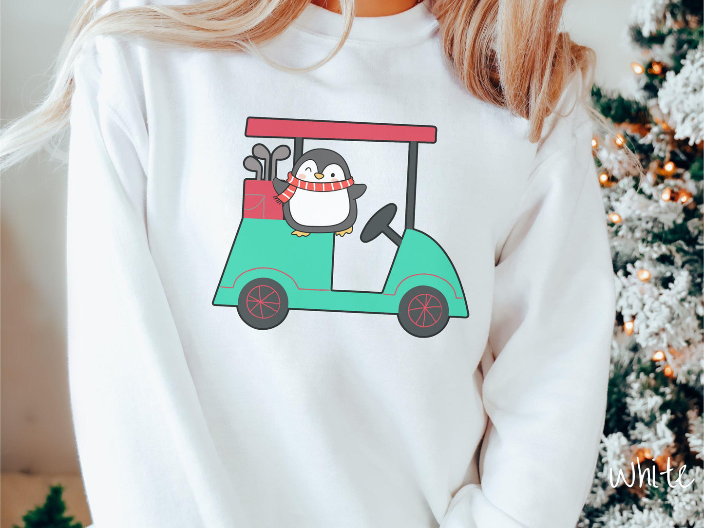 A woman wearing a cute white colored sweatshirt with smiling penguin driving a green golf cart and waving with both hands.