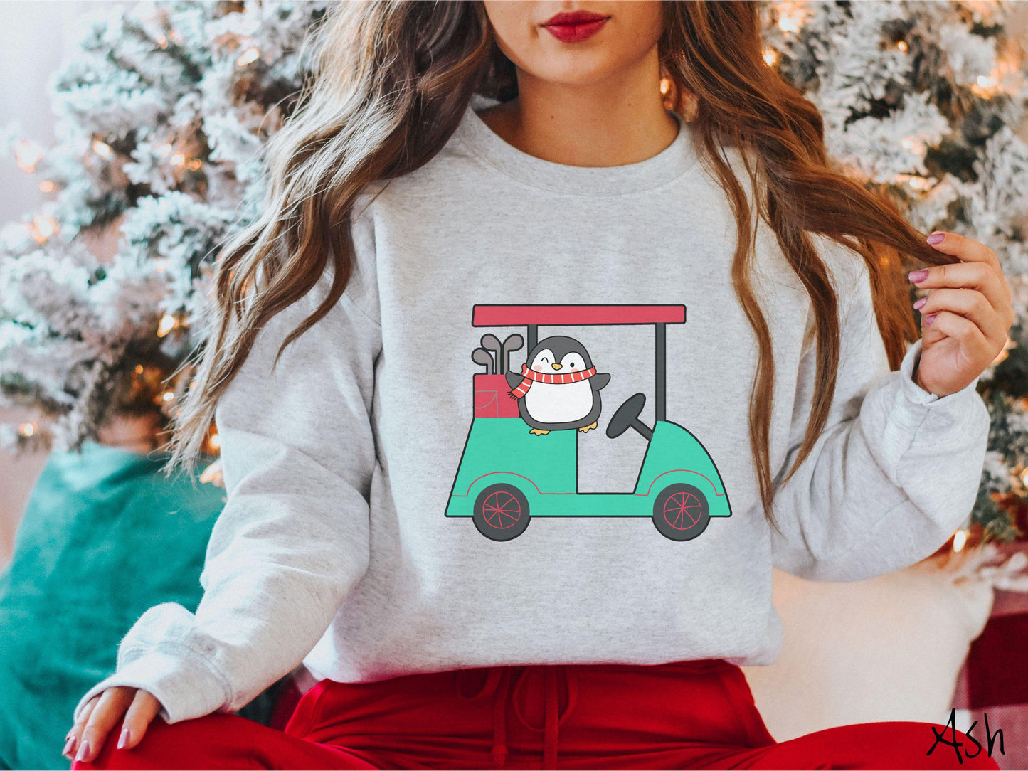 A woman wearing a cute ash colored sweatshirt with smiling penguin driving a green golf cart and waving with both hands.