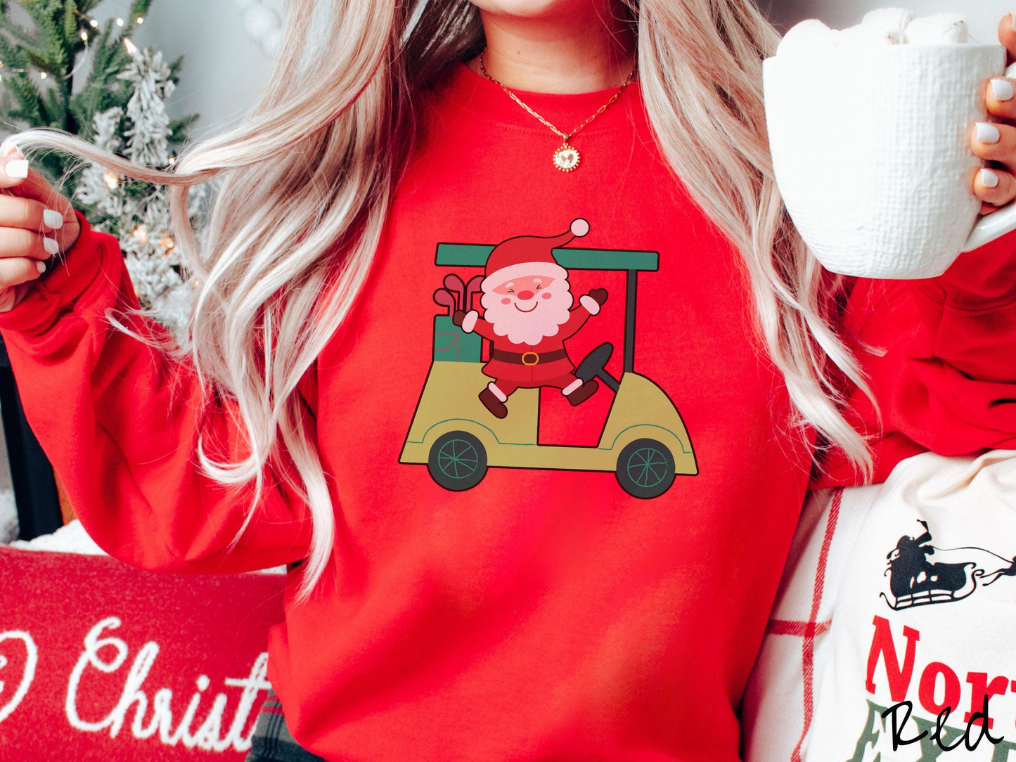 A woman wearing a cute red colored sweatshirt with smiling Santa driving a green golf cart and waving with both hands.