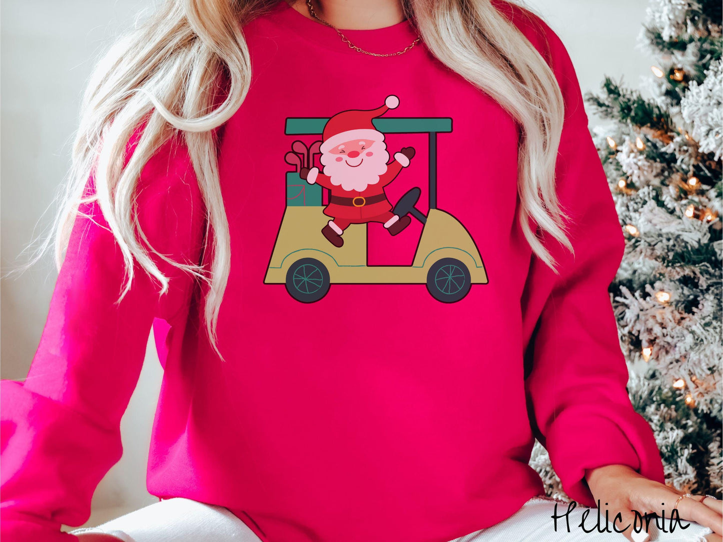 A woman wearing a cute heliconia colored sweatshirt with smiling Santa driving a green golf cart and waving with both hands.