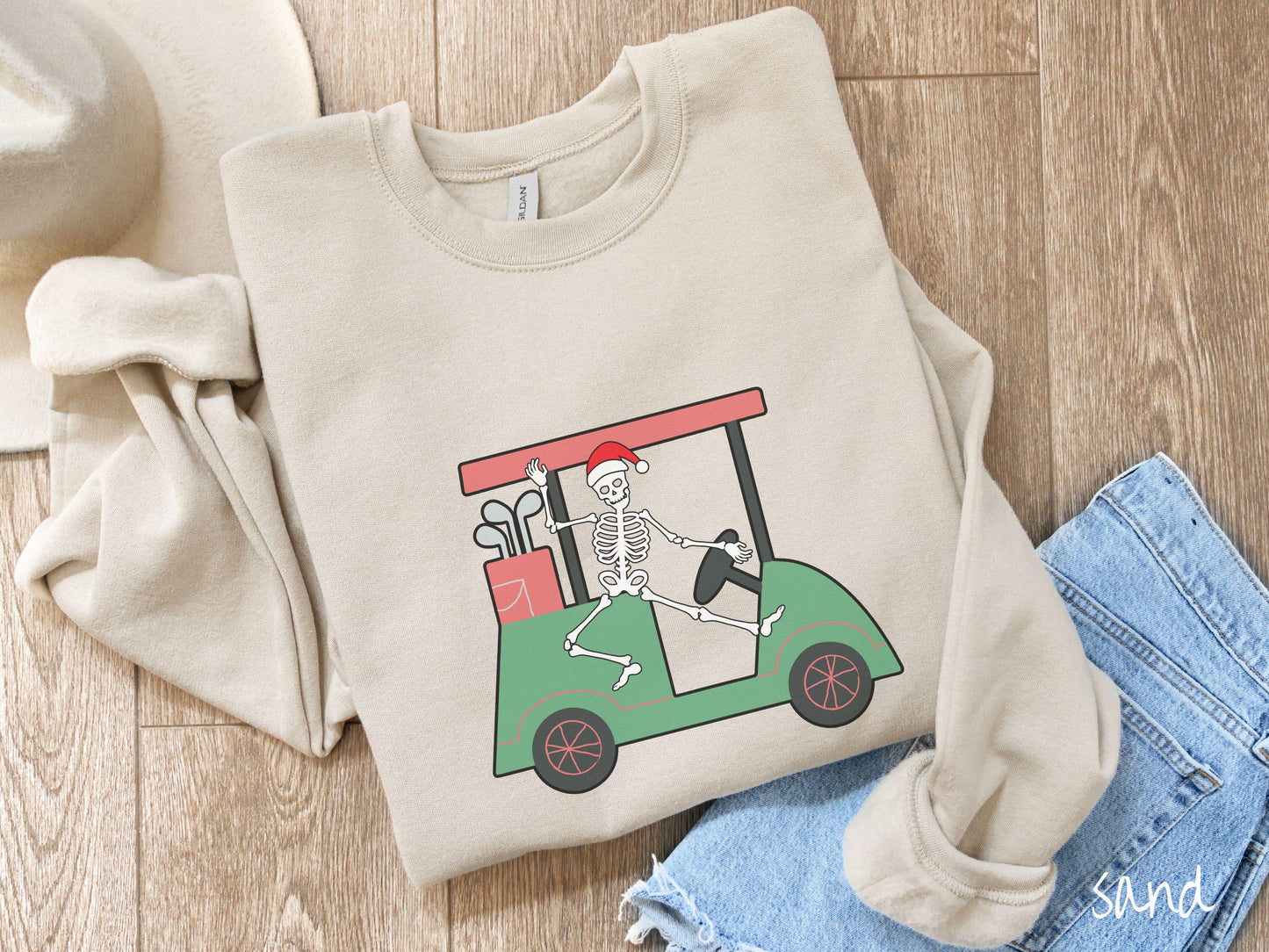 A woman wearing a cute sand colored sweatshirt with smiling Skeleton with a Santa Hat driving a green golf cart and waving with one hand