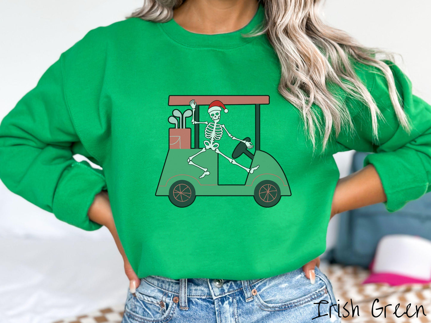 A woman wearing a cute irish green colored sweatshirt with smiling Skeleton with a Santa Hat driving a green golf cart and waving with one hand