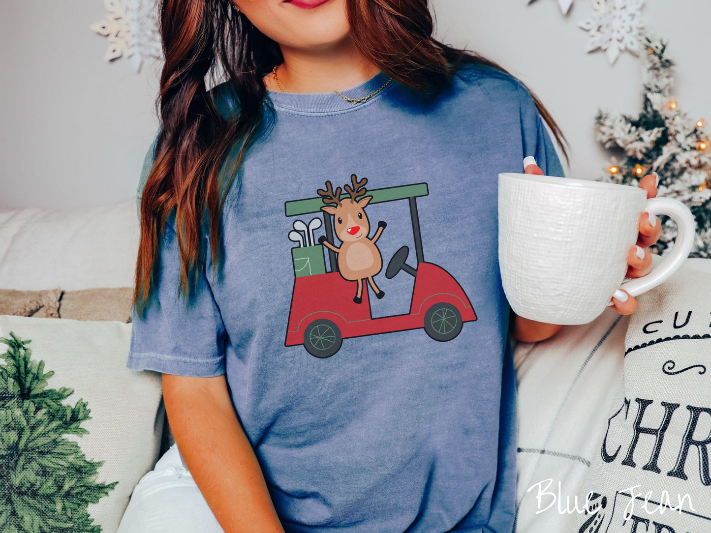 A woman wearing a cute blue jean colored shirt with smiling reindeer driving a red golf cart and waving with both hands.