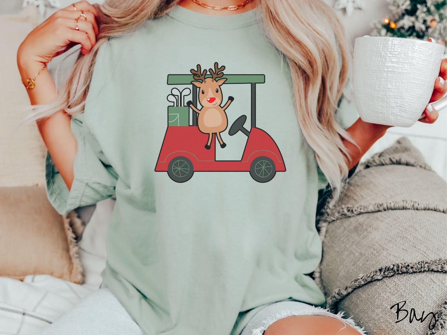 A woman wearing a cute bay colored shirt with smiling reindeer driving a red golf cart and waving with both hands.