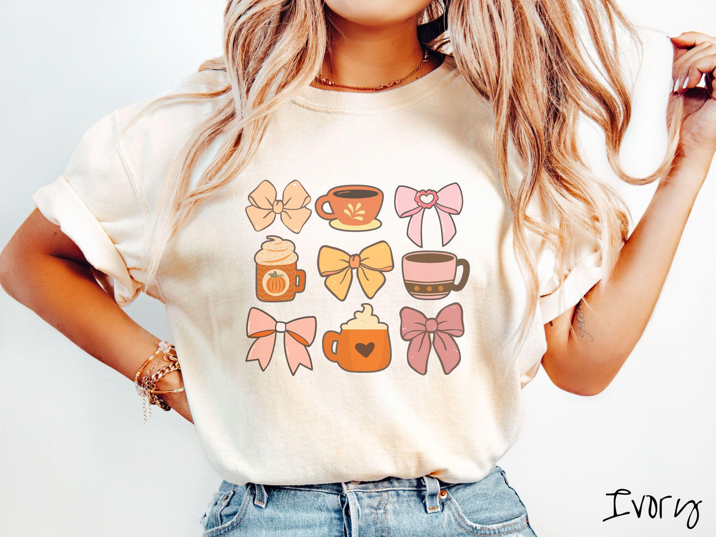 A woman wearing a cute, vintage ivory colored Comfort Colors T-shirt with a grid of pictures of an orange bow, an orange tea cup, a pink bow, an orange pumpkin-spiced latte, a yellow bow, a pink coffee cup, a pink bow, and an orange coffee drink.