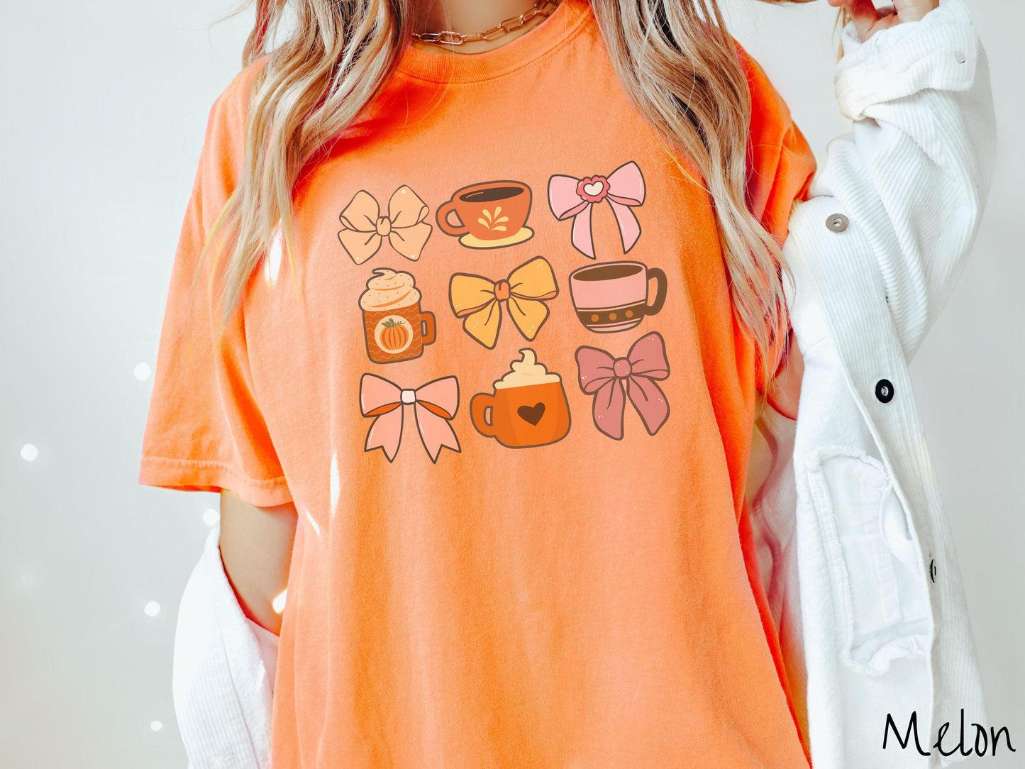 A woman wearing a cute, vintage melon colored Comfort Colors T-shirt with a grid of pictures of an orange bow, an orange tea cup, a pink bow, an orange pumpkin-spiced latte, a yellow bow, a pink coffee cup, a pink bow, and an orange coffee drink.