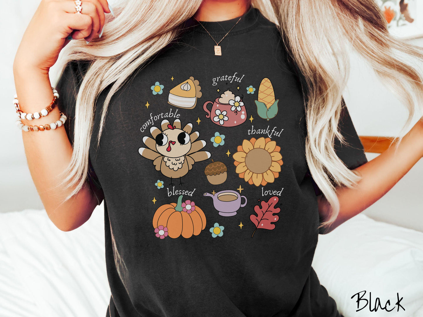 A woman wearing a cute, vintage black colored Comfort Colors T-shirt with text grateful comfortable thankful blessed and love. In a grid format are a piece of pumpkin pie, a coffee mug, corn, a turkey, a sunflower, a pumpkin, a leaf, and an acorn.