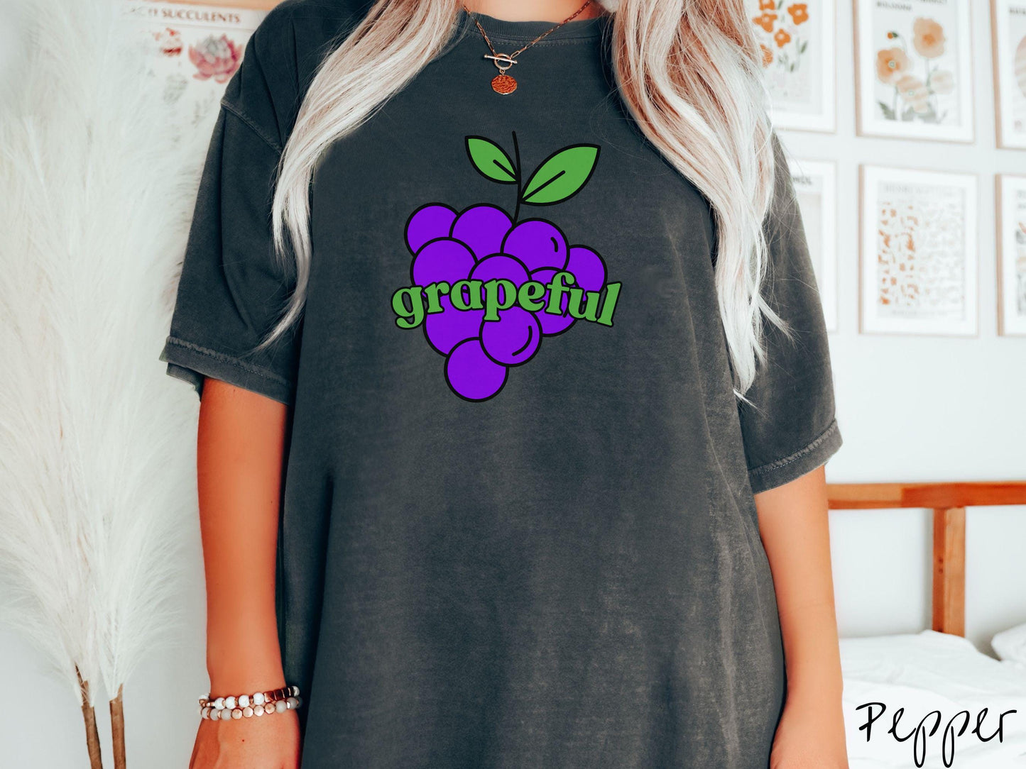 A woman wearing a cute, vintage pepper colored Comfort Colors T-shirt with the text grapeful in green font across the front. Behind grapeful is a bunch of juicy, purple grapes with a green stem.