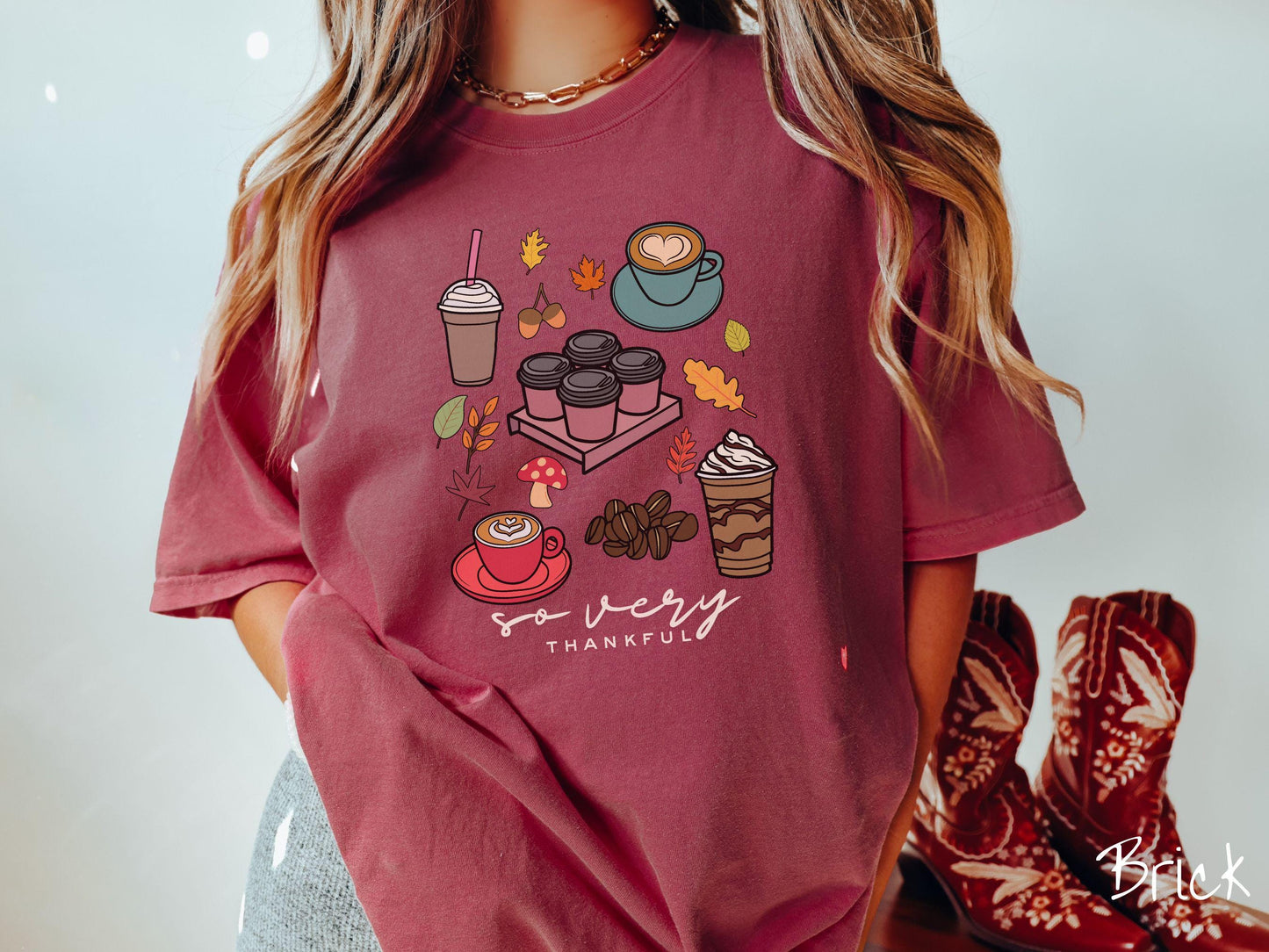 A woman wearing a cute, vintage brick colored Comfort Colors T-shirt with the text so very thankful. Above are an iced coffee, four to-go cup coffees, a latte, a frappucino, coffee beans, mushrooms, and fall leaves scattered around.
