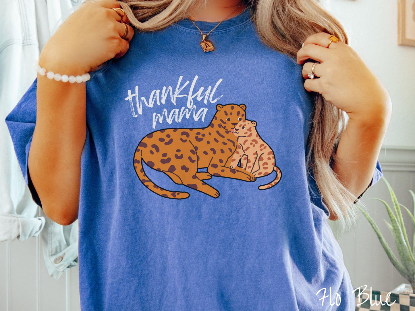 A woman wearing a cute, vintage flo blue colored Comfort Colors T-shirt with the text thankful mama in black, sharpie font. Below is an orange, mother leopard coddling its child.