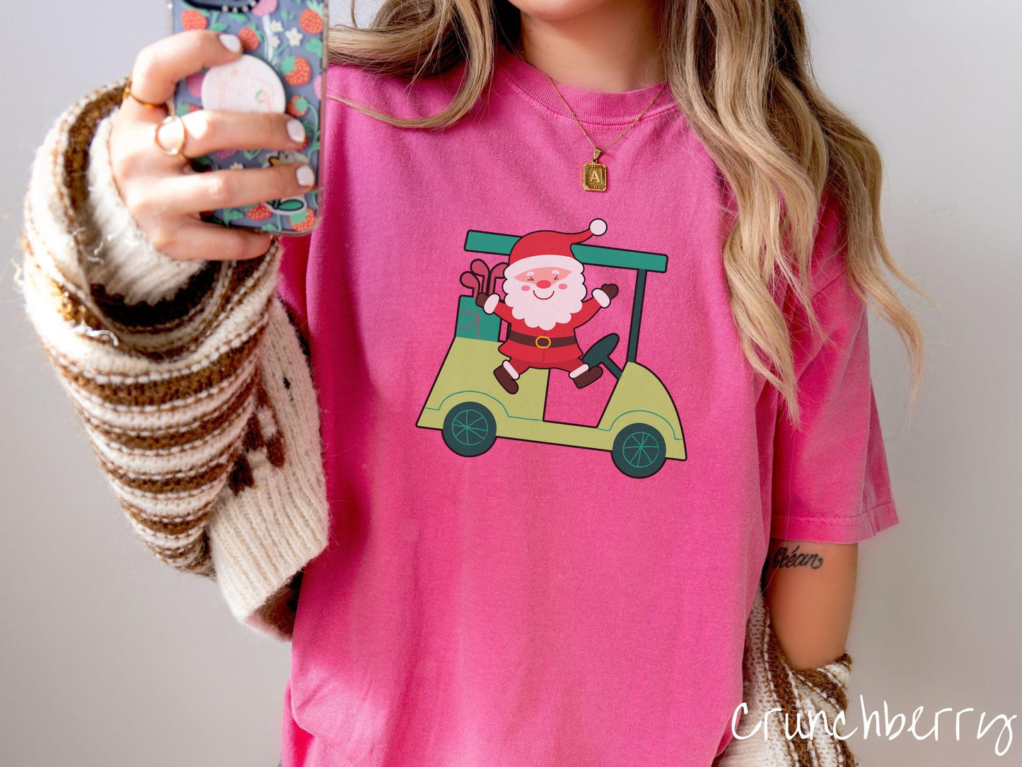 A woman wearing a cute crunchberry colored shirt with smiling Santa driving a green golf cart and waving with both hands.