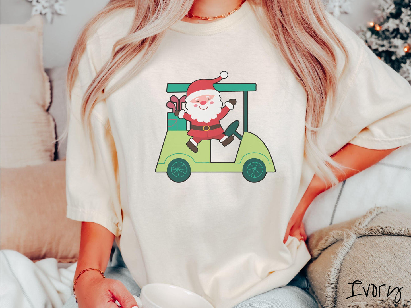 A woman wearing a cute ivory colored shirt with smiling Santa driving a green golf cart and waving with both hands.