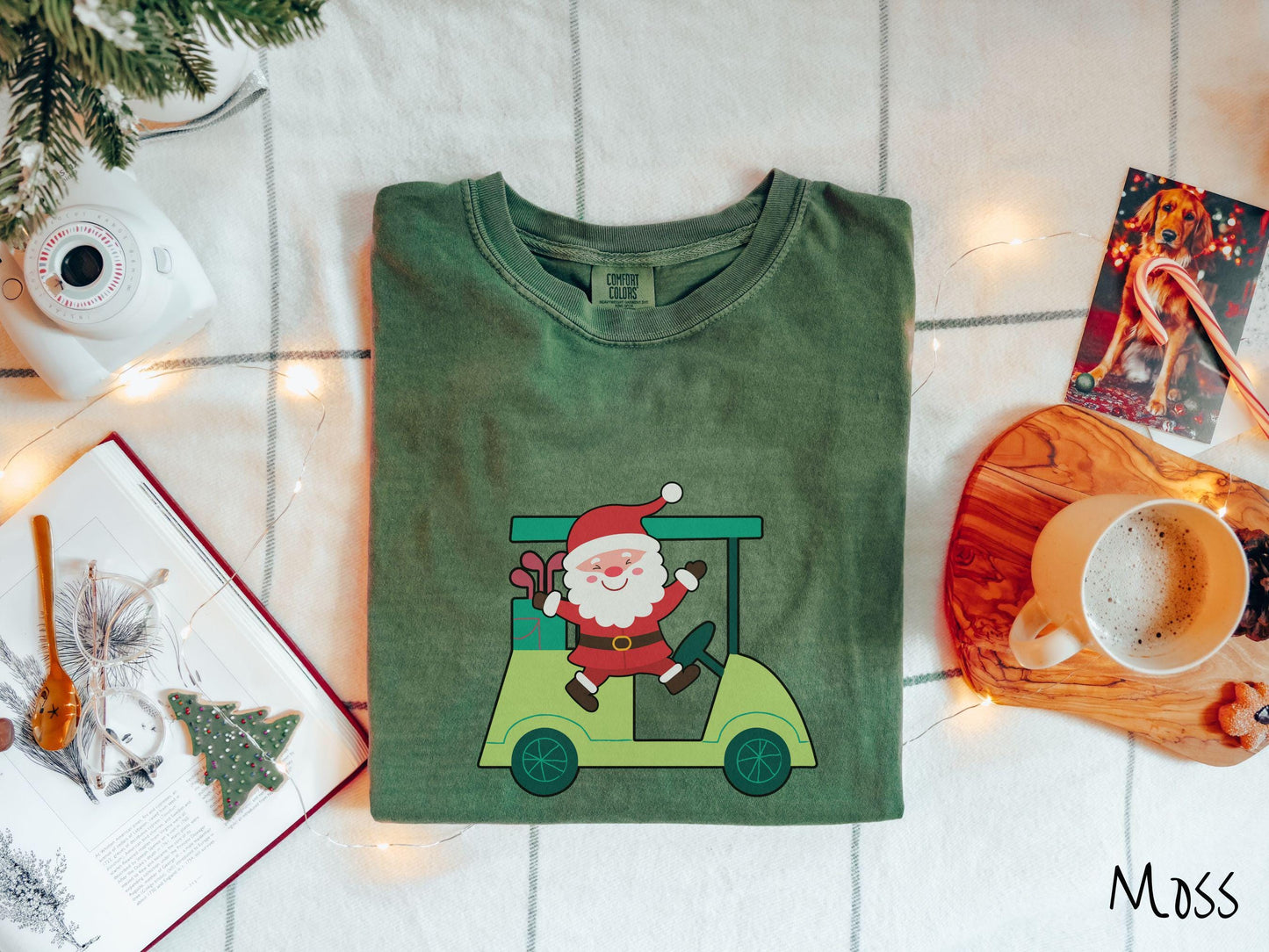 A woman wearing a cute moss colored shirt with smiling Santa driving a green golf cart and waving with both hands.