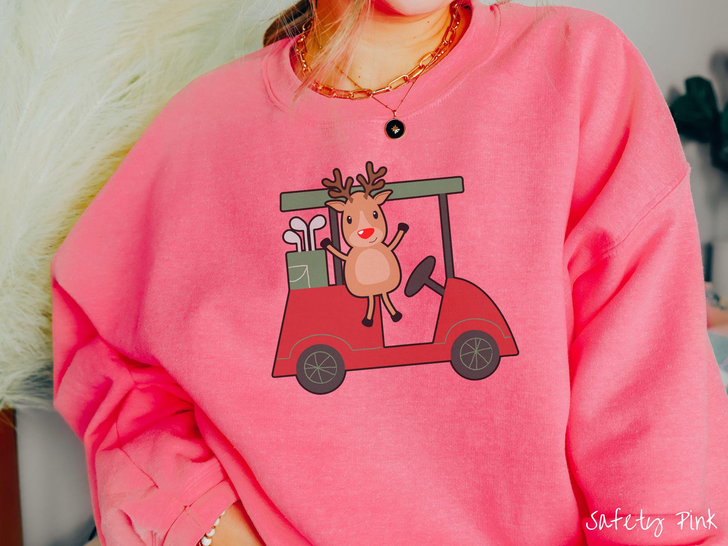 A woman wearing a cute safety pink colored sweatshirt with smiling reindeer driving a red golf cart and waving with both hands.