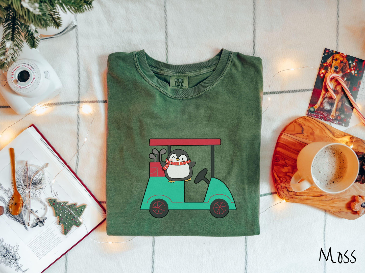 A woman wearing a cute moss colored shirt with smiling penguin driving a green golf cart and waving with both hands.