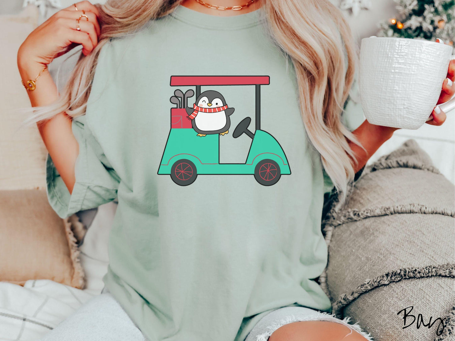 A woman wearing a cute bay colored shirt with smiling penguin driving a green golf cart and waving with both hands.
