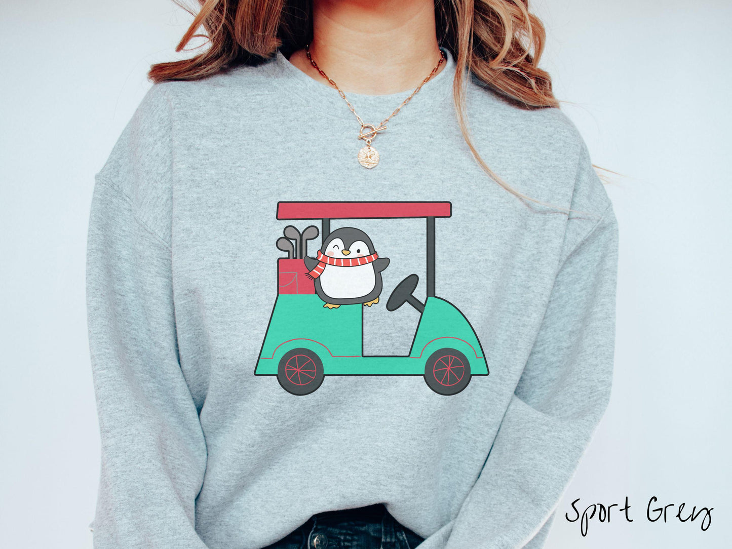 A woman wearing a cute sport grey colored sweatshirt with smiling penguin driving a green golf cart and waving with both hands.