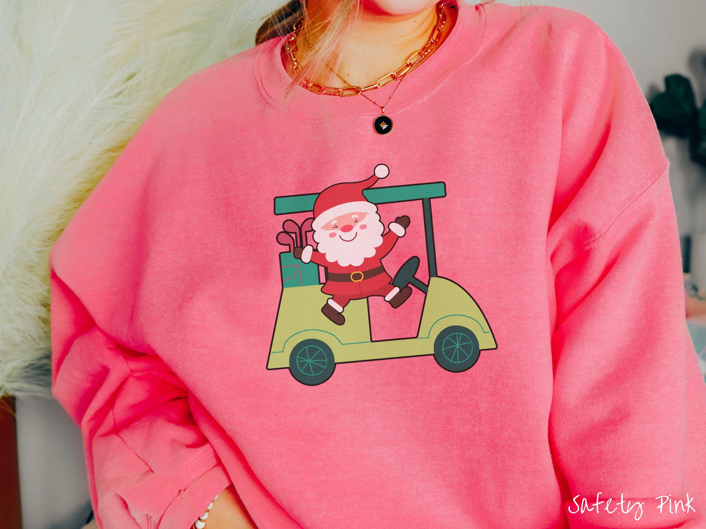 A woman wearing a cute safety pink colored sweatshirt with smiling Santa driving a green golf cart and waving with both hands.