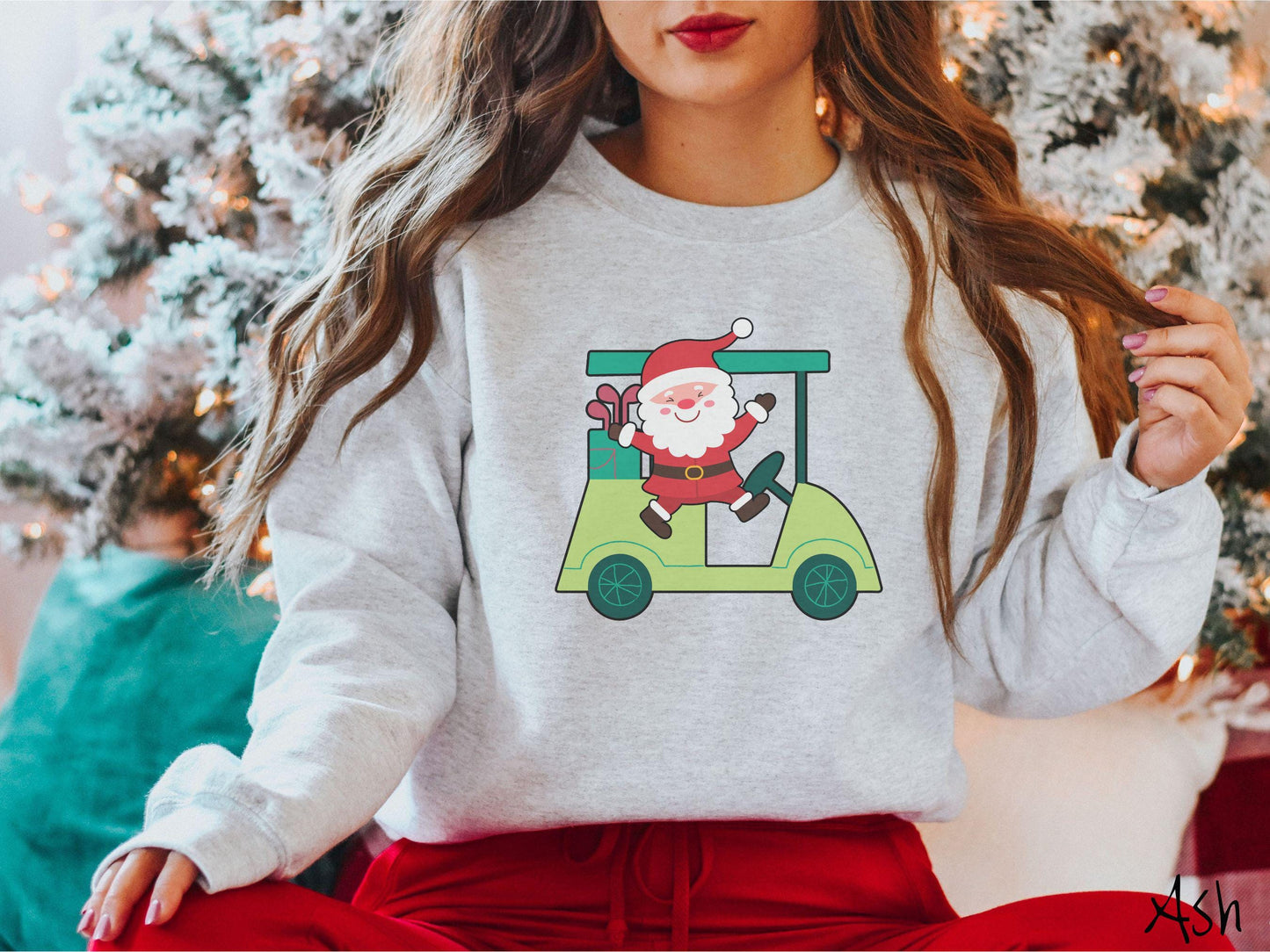 A woman wearing a cute ash colored sweatshirt with smiling Santa driving a green golf cart and waving with both hands.