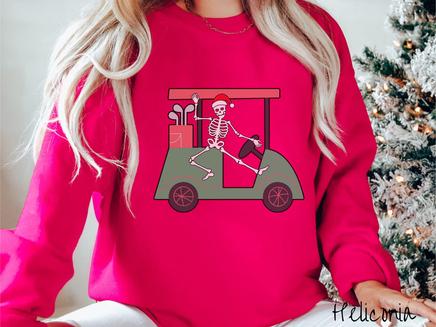 A woman wearing a cute heliconia colored sweatshirt with smiling Skeleton with a Santa Hat driving a green golf cart and waving with one hand