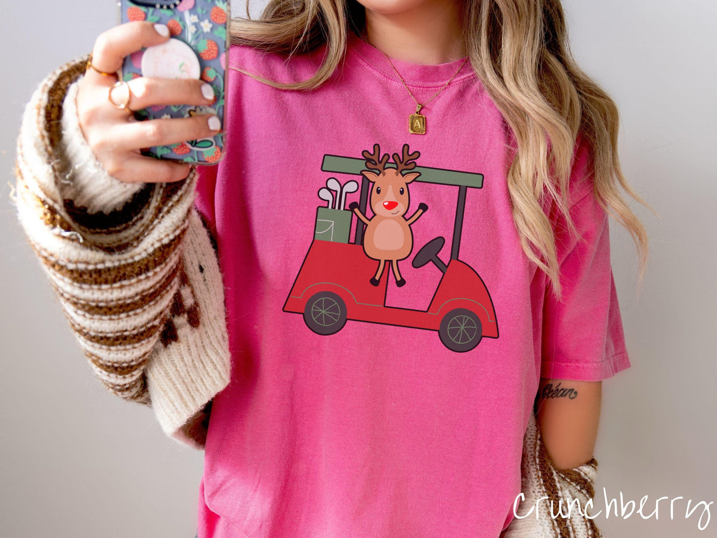 A woman wearing a cute crunchberry colored shirt with smiling reindeer driving a red golf cart and waving with both hands.