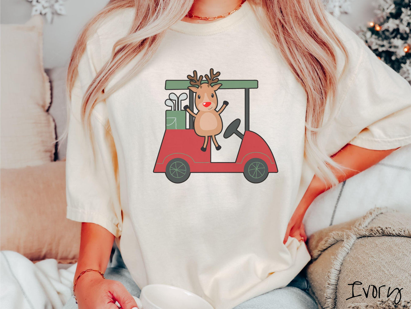 A woman wearing a cute ivory colored shirt with smiling reindeer driving a red golf cart and waving with both hands.