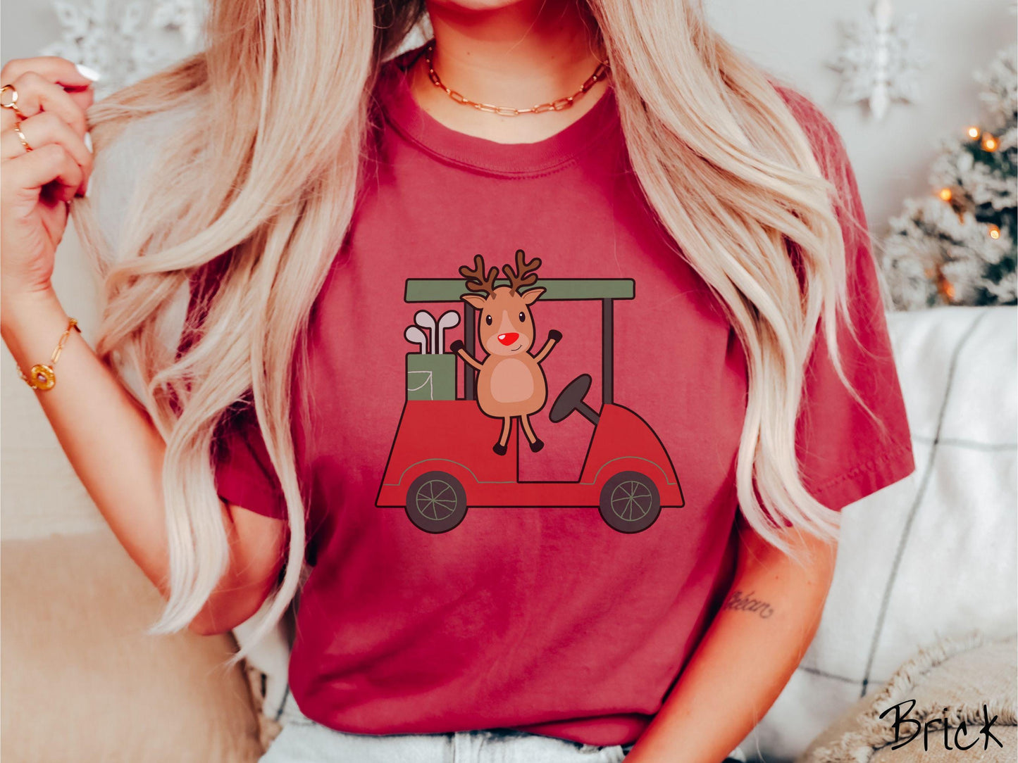 A woman wearing a cute brick colored shirt with smiling reindeer driving a red golf cart and waving with both hands.