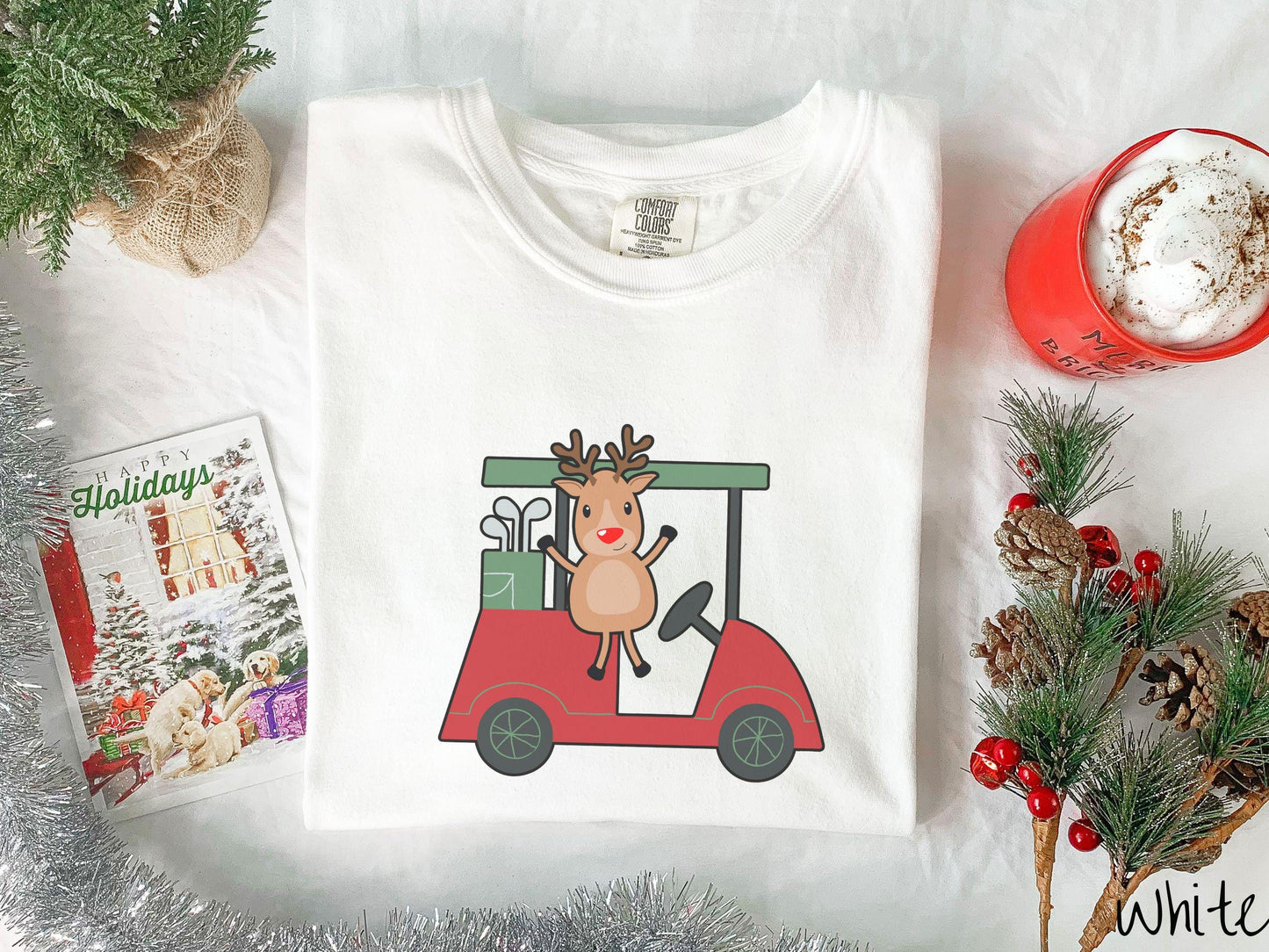 A woman wearing a cute white colored shirt with smiling reindeer driving a red golf cart and waving with both hands.