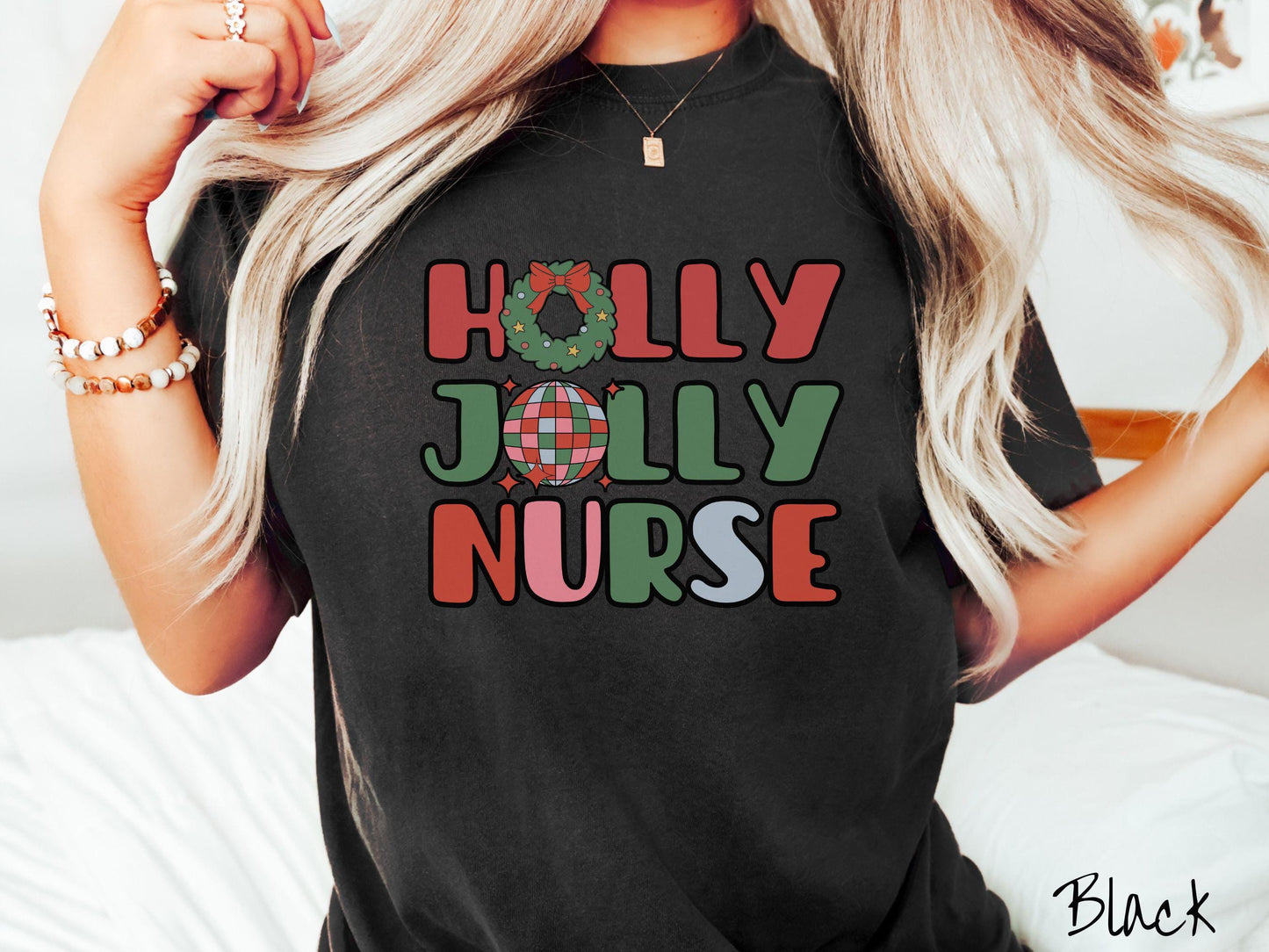 A woman wearing a cute, vintage black colored Comfort Colors T-shirt with text Holly Jolly Nurse in red, green , pink, and cadet blue font. The letter O in Holly is a Christmas wreath and the letter O in Jolly is a red, green, and blue disco ball.