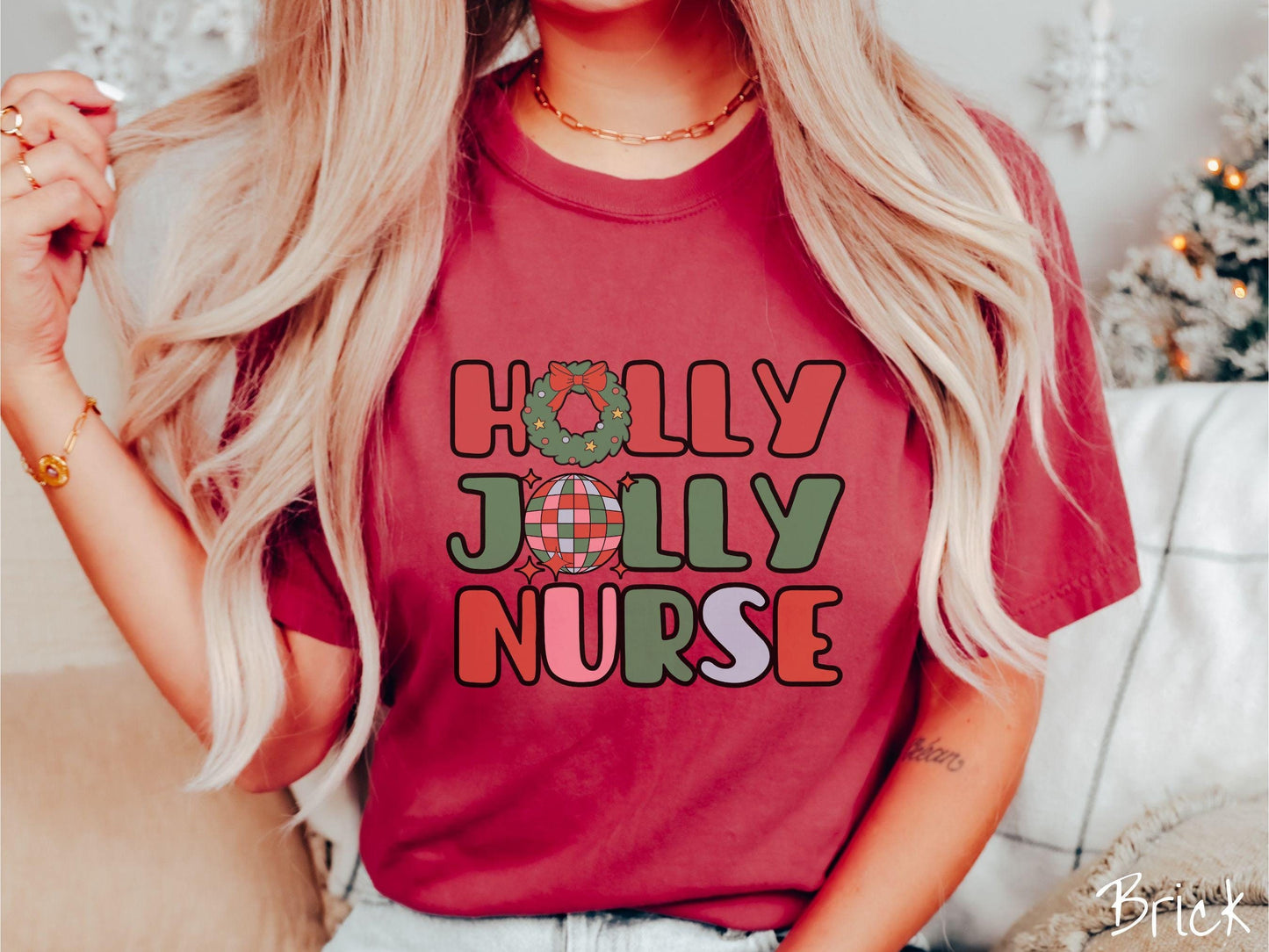 A woman wearing a cute, vintage brick colored Comfort Colors T-shirt with text Holly Jolly Nurse in red, green , pink, and cadet blue font. The letter O in Holly is a Christmas wreath and the letter O in Jolly is a red, green, and blue disco ball.