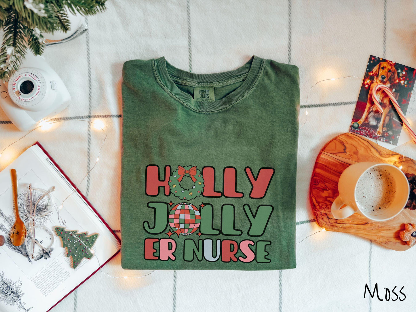 A cute, vintage moss colored Comfort Colors T-shirt with the text Holly Jolly ER Nurse in red, green, pink, and blue font. The letter O in Holly is a Christmas wreath and the letter O in Jolly is a multi-colored disco ball.