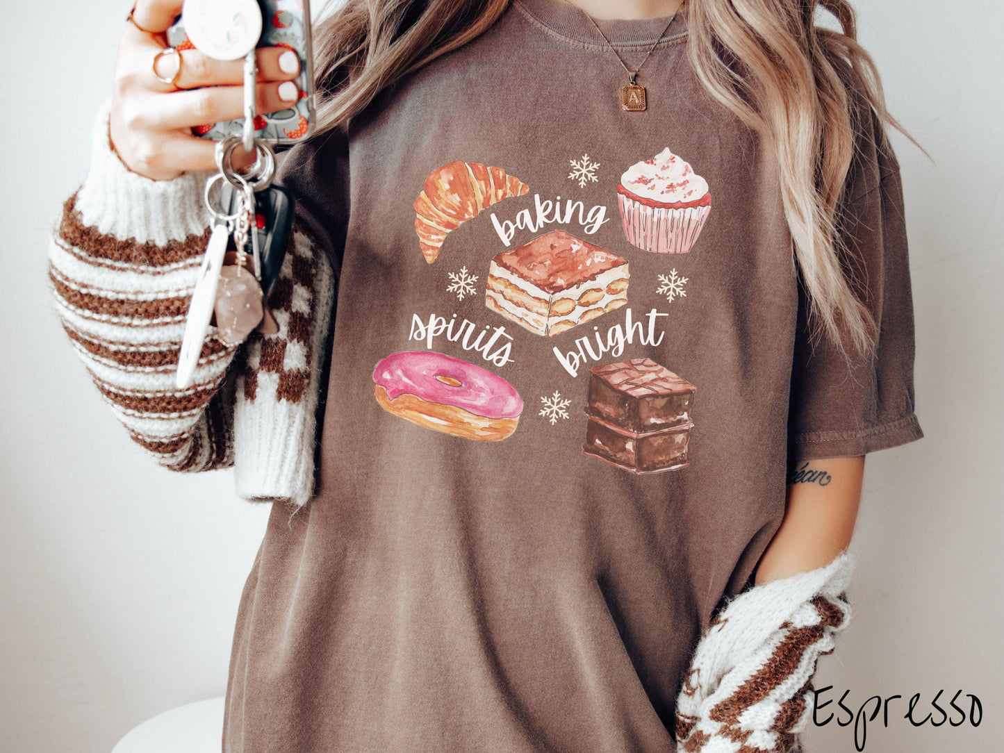This vintage espresso colored Comfort Colors T-shirt features the text 'baking spirits bright' in white cursive font, accompanied by cute dessert illustrations and white snowflakes.