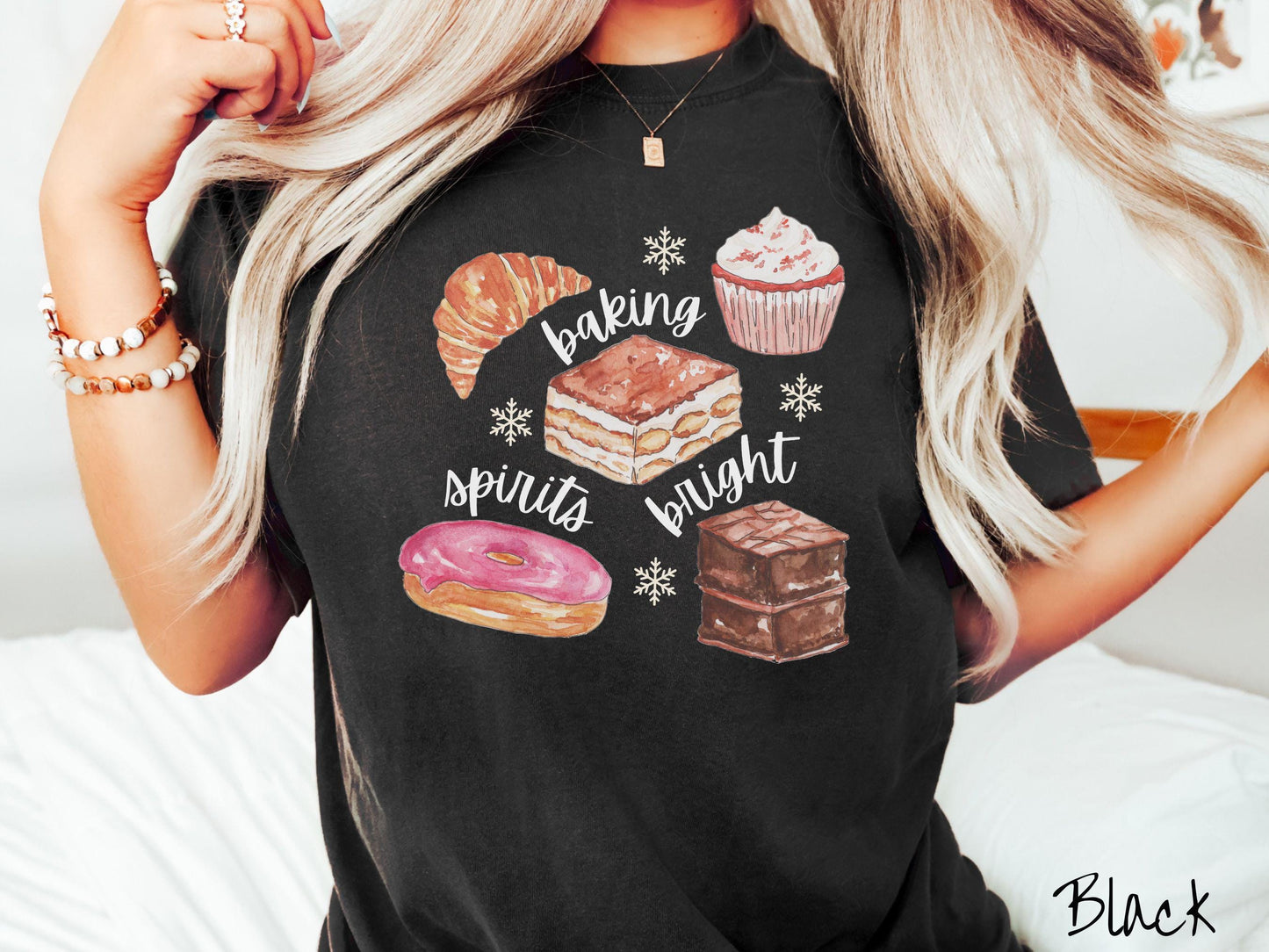 This vintage black colored Comfort Colors T-shirt features the text 'baking spirits bright' in white cursive font, accompanied by cute dessert illustrations and white snowflakes.