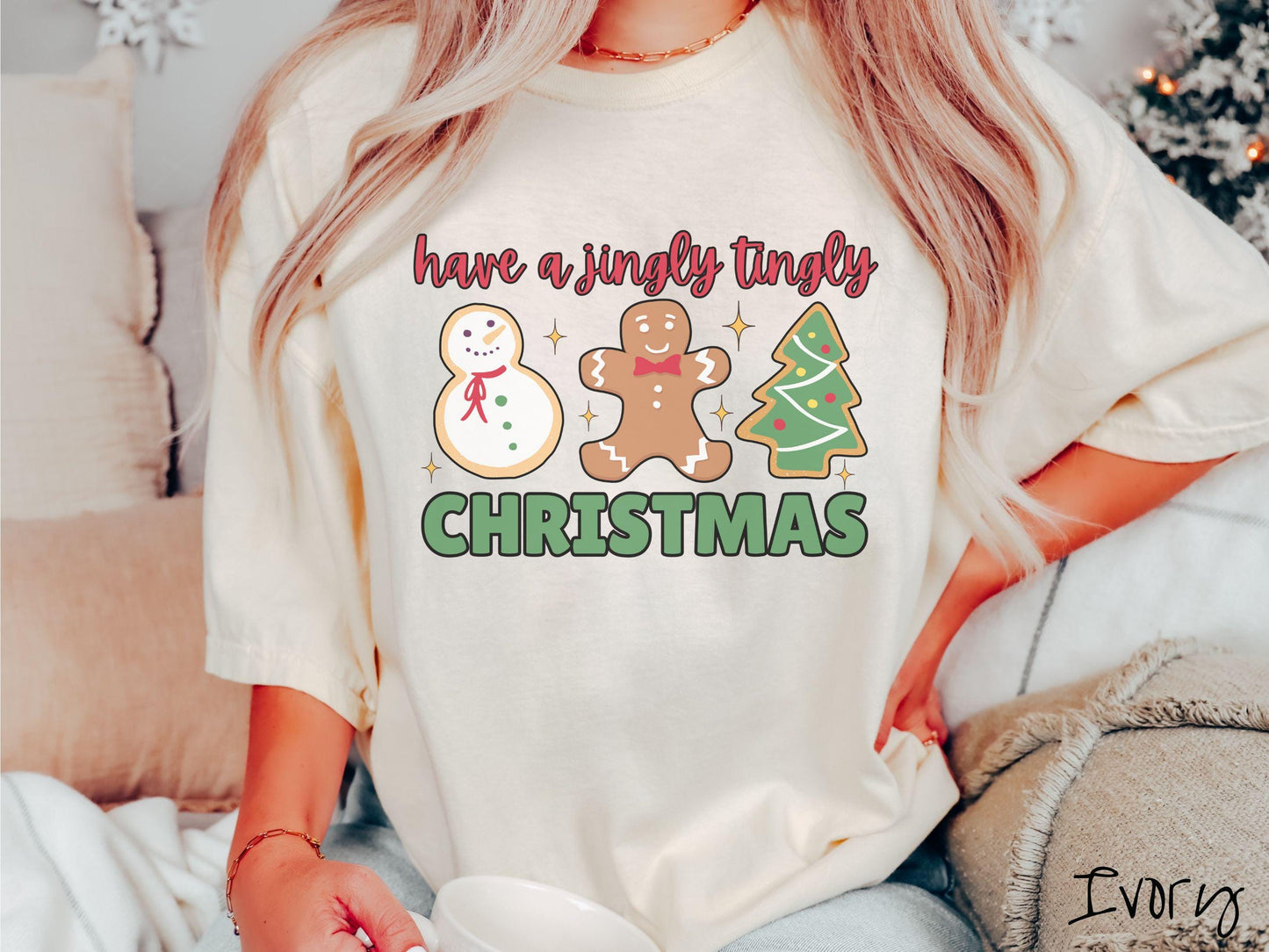 A vintage ivory colored Christmas Comfort Colors t-shirt featuring a snowman iced cookie, a gingerbread man cookie, and a Christmas tree cookie. The text reads 'have a jingly tingly Christmas' in red and green font.