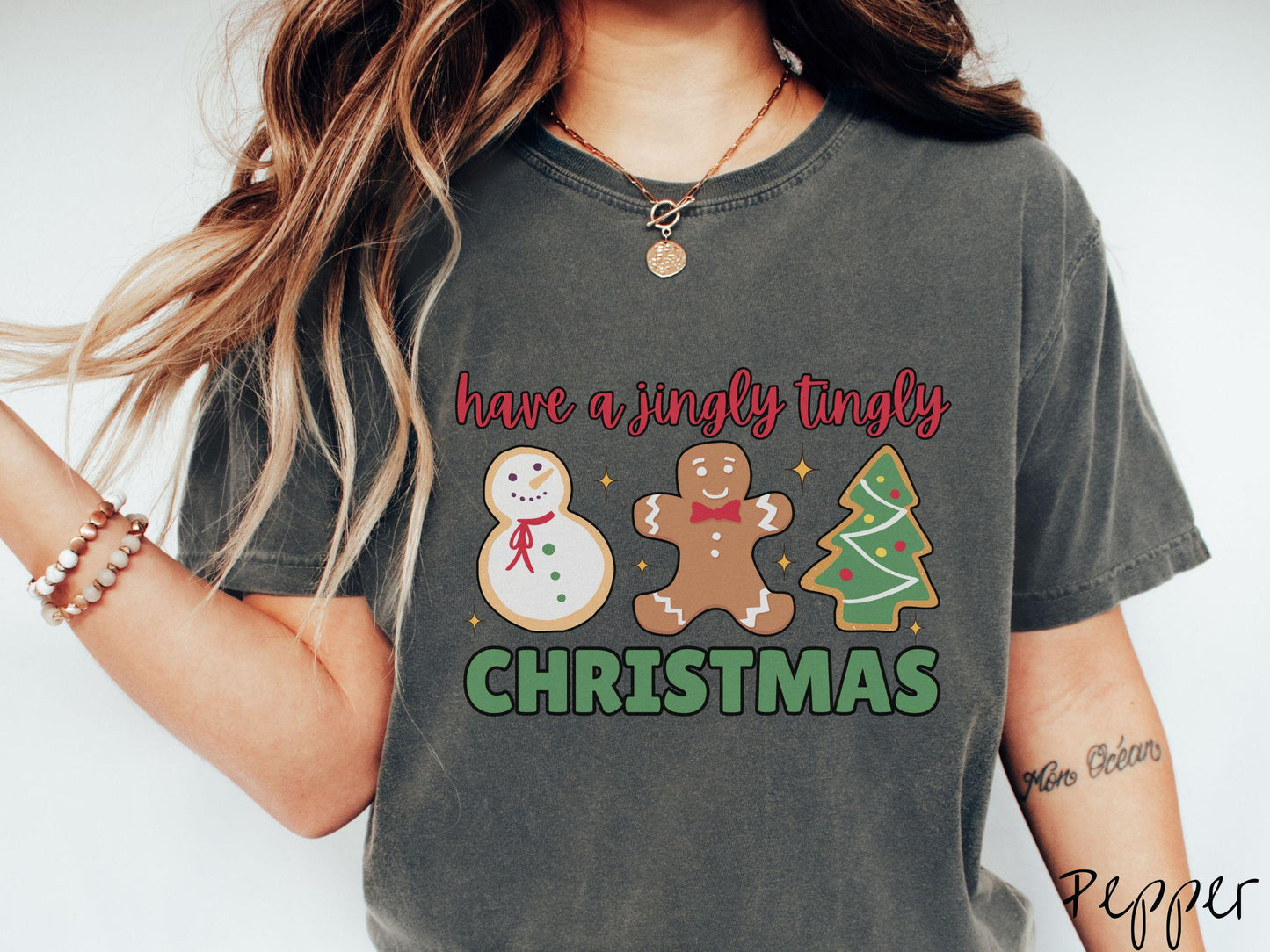 A vintage pepper colored Christmas Comfort Colors t-shirt featuring a snowman iced cookie, a gingerbread man cookie, and a Christmas tree cookie. The text reads 'have a jingly tingly Christmas' in red and green font.