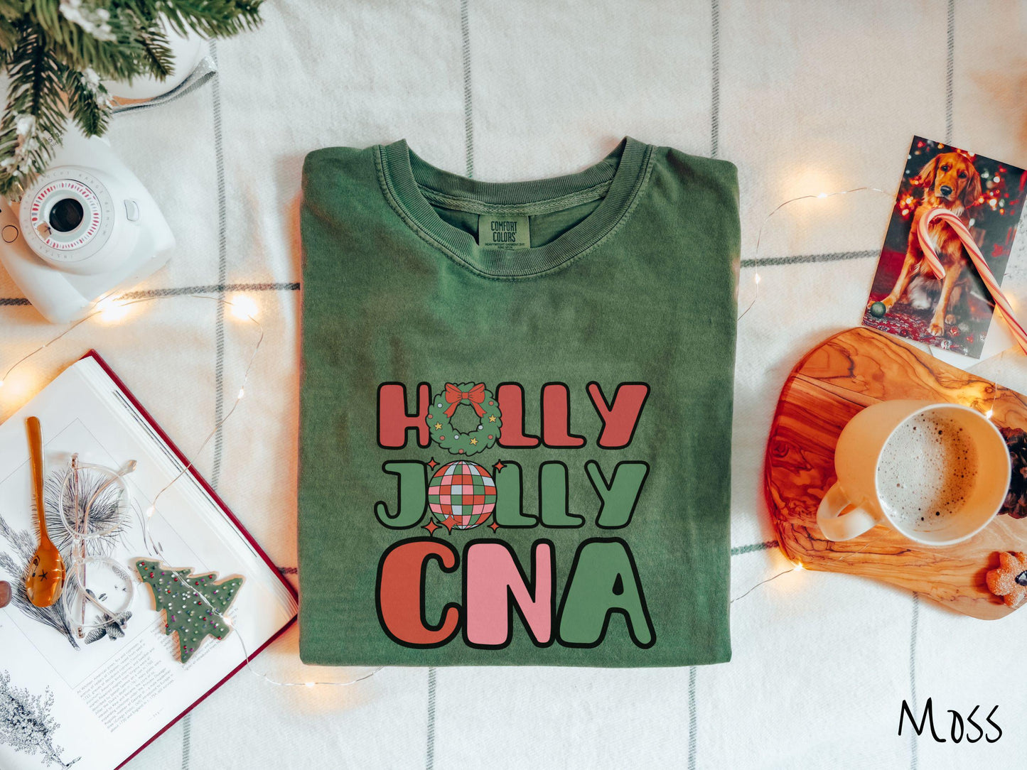 A cute, vintage brick colored Comfort Colors T-shirt with the text Holly Jolly CNA in red, green, pink, and blue font. The letter O in Holly is a Christmas wreath and the letter O in Jolly is a multi-colored disco ball.